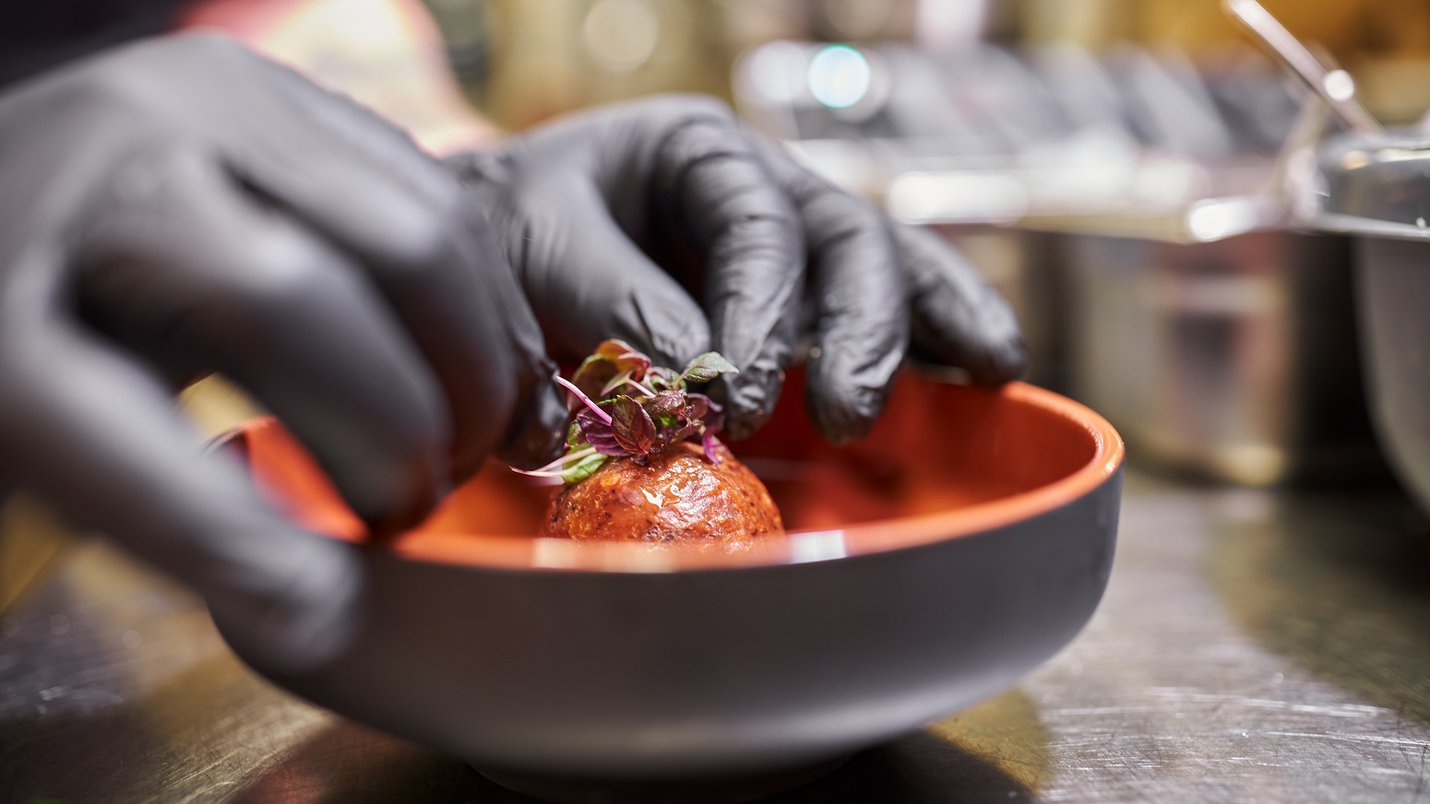 Hotel Sonnenhof Koch mit schwarzen Handschuhen richtet eine kleine Fleischbällchen-Garnierung an.