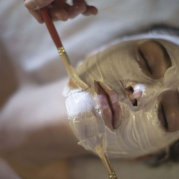Hotel Sonnenhof Person mit geschlossenen Augen bekommt eine weiße Gesichtsmaske mit Pinsel aufgetragen