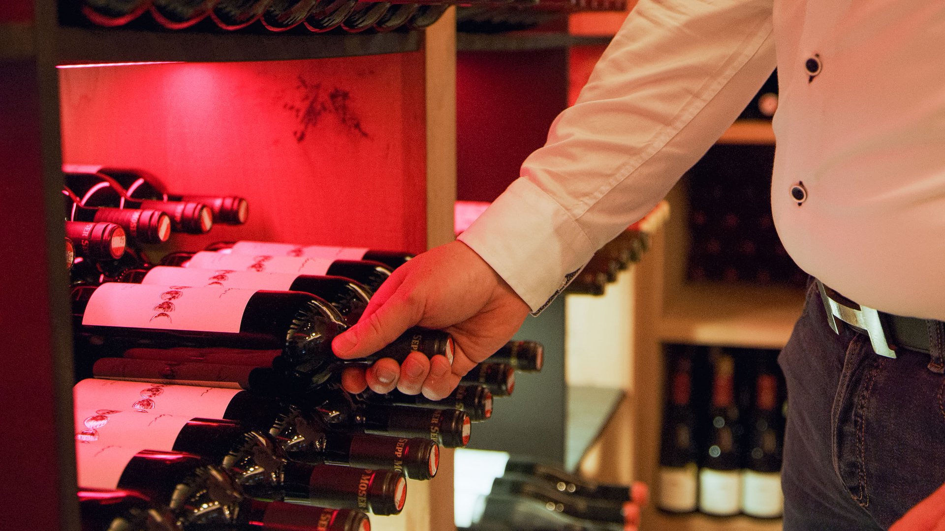 Hotel Sonnenhof Hand grabbing a wine bottle from a red-lit wine rack