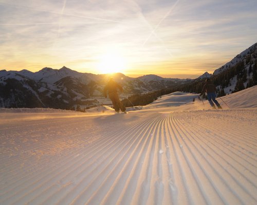 Hotel Sonnenhof Skifahrer fahren bei Sonnenuntergang auf frisch präparierter Piste in den Bergen
