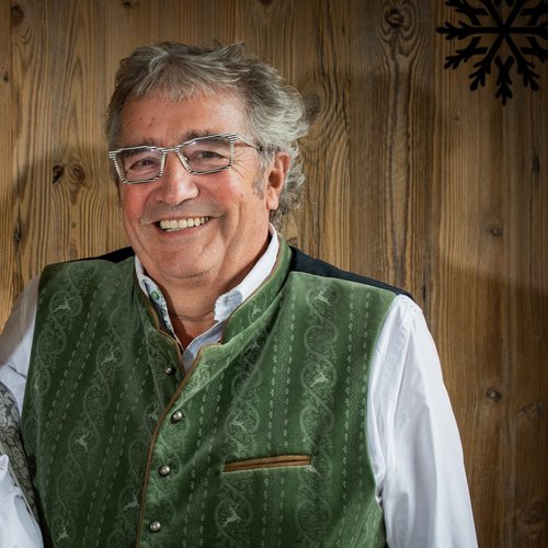 Hotel Sonnenhof Older couple in traditional Bavarian clothing in front of wooden wall