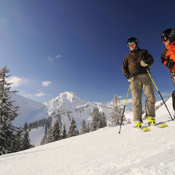 Hotel Sonnenhof Zwei Skifahrer auf schneebedecktem Hang mit Bergen und Bäumen im Hintergrund