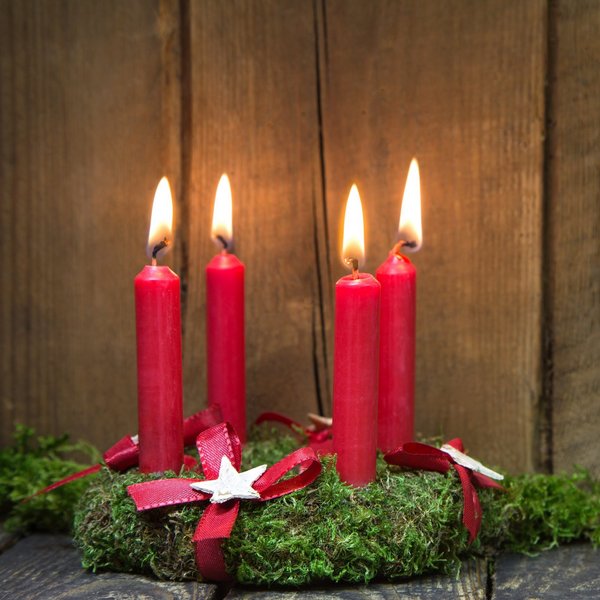 Hotel Sonnenhof Adventskranz mit vier roten brennenden Kerzen auf Holz und Moos
