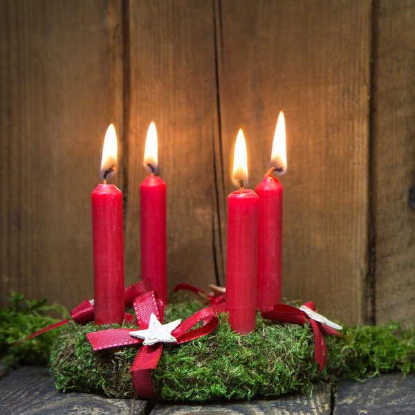 Hotel Sonnenhof Adventskranz mit vier roten brennenden Kerzen auf Holz und Moos