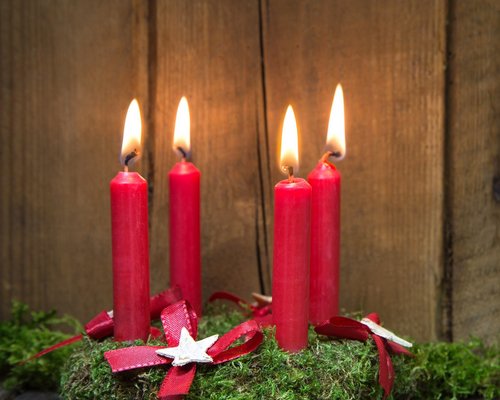 Hotel Sonnenhof Adventskranz mit vier roten brennenden Kerzen auf Holz und Moos
