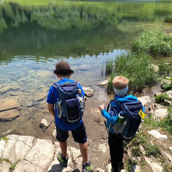 Hotel Sonnenhof Zwei Jungen mit Rucksäcken stehen am Ufer eines klaren Bergsees