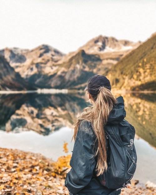 Hotel Sonnenhof Frau mit schwarzem Rucksack blickt auf ruhigen Bergsee mit Spiegelung