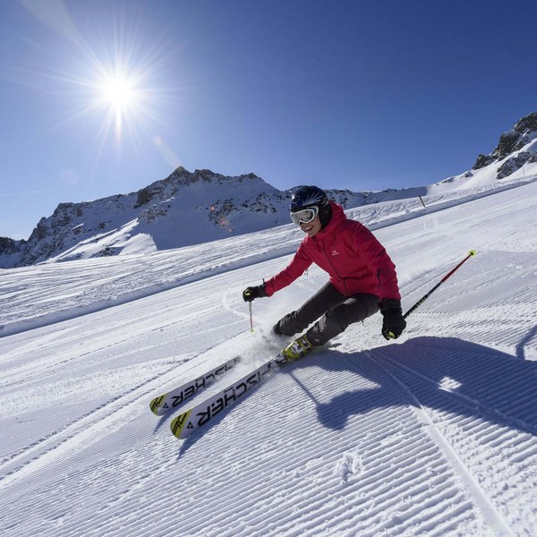 Hotel Sonnenhof Skifahrer in roter Jacke fährt bei Sonnenschein auf präparierter Piste