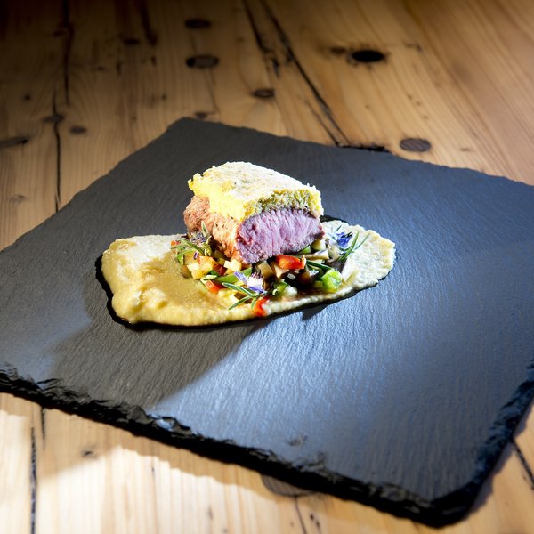 Hotel Sonnenhof Gourmetgericht mit rosa gebratenem Fleisch, Gemüse und Püree auf schwarzer Steintafel