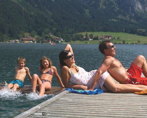 Hotel Sonnenhof Familie entspannt am Seeufer auf Steg mit Bergen und Häusern im Hintergrund