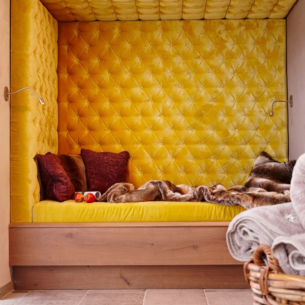 Hotel Sonnenhof Gelbe gepolsterte Sitzecke mit roten Kissen und Decke in modernem Raum