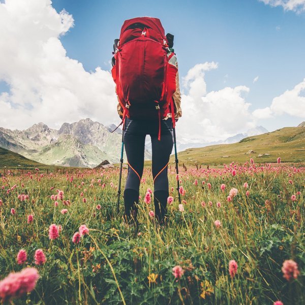 Hotel Sonnenhof Wanderer mit rotem Rucksack in einem blühenden Tal vor Bergen