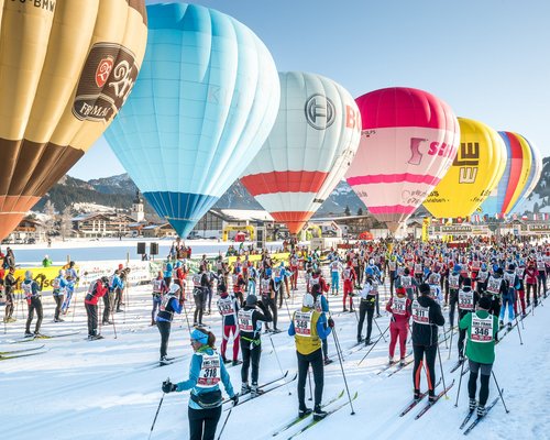 Hotel Sonnenhof Skilangläufer starten im Schnee unter bunten Heißluftballons bei klarem Himmel