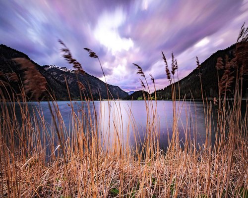 Hotel Sonnenhof See mit Schilf vor Bergen und bewölktem dramatischem Himmel bei Sonnenuntergang