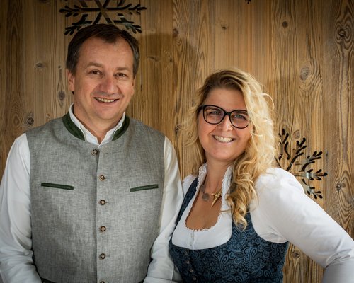 Hotel Sonnenhof Lächelnder Mann und Frau in traditioneller Kleidung vor Holzvertäfelung