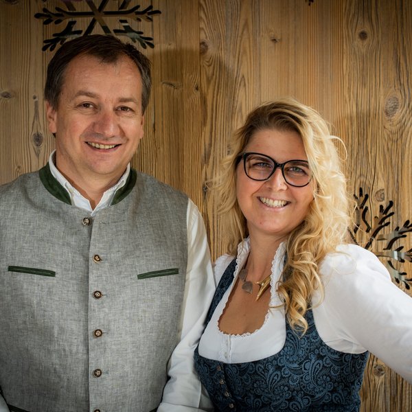 Hotel Sonnenhof Lächelnder Mann und Frau in traditioneller Kleidung vor Holzvertäfelung