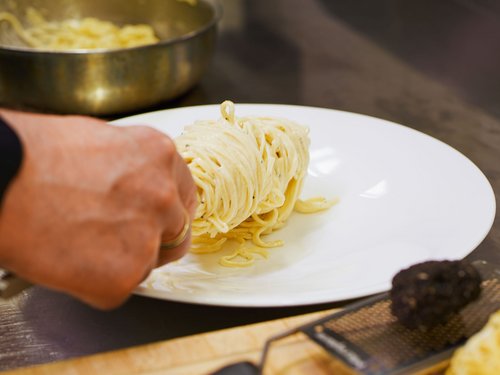 Hotel Sonnenhof Hand with spoon serving a portion of spaghetti on white plate in kitchen