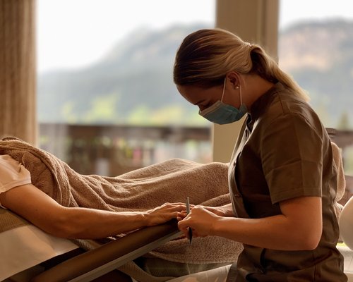 Hotel Sonnenhof Frau mit Maske macht Maniküre während Kunde entspannt auf Liegestuhl liegt